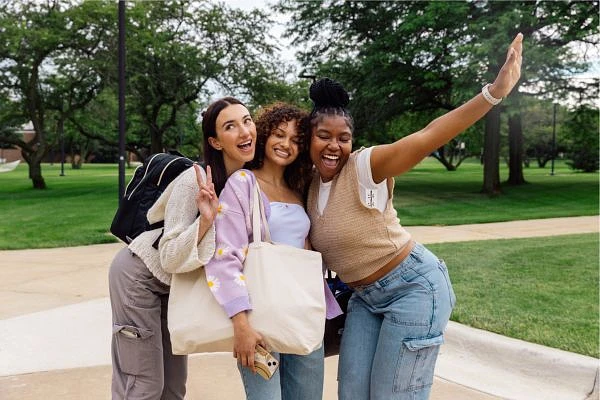 Three friends pose happily together outdoors with trees in the background.