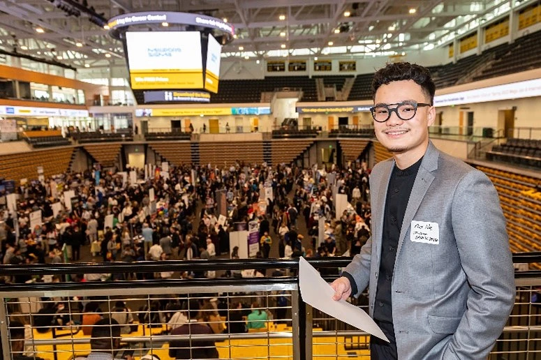Person in blazer standing in front of career fair activities in progress