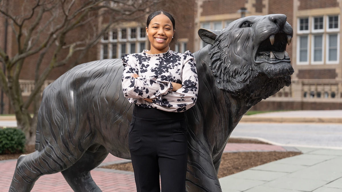 A person stands smiling with arms crossed next to a large statue of a roaring tiger.